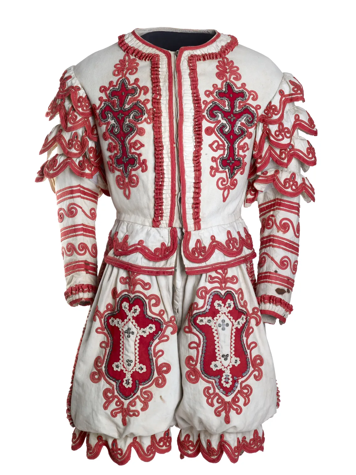 Traditional folk costume with elaborate red and black embroidery on white fabric, featuring ruffled sleeves and decorative belt details.