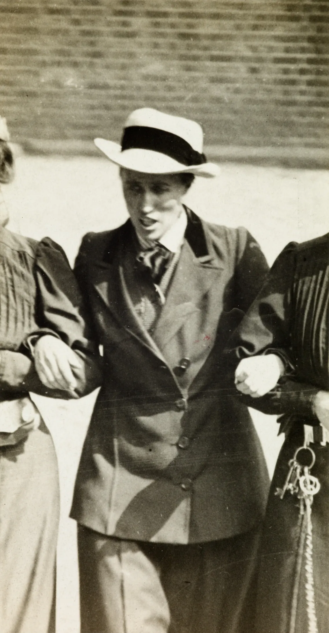 Vintage black-and-white photo of a person wearing a suit and hat, engaging in conversation beside a figure partially visible to the left, near water.