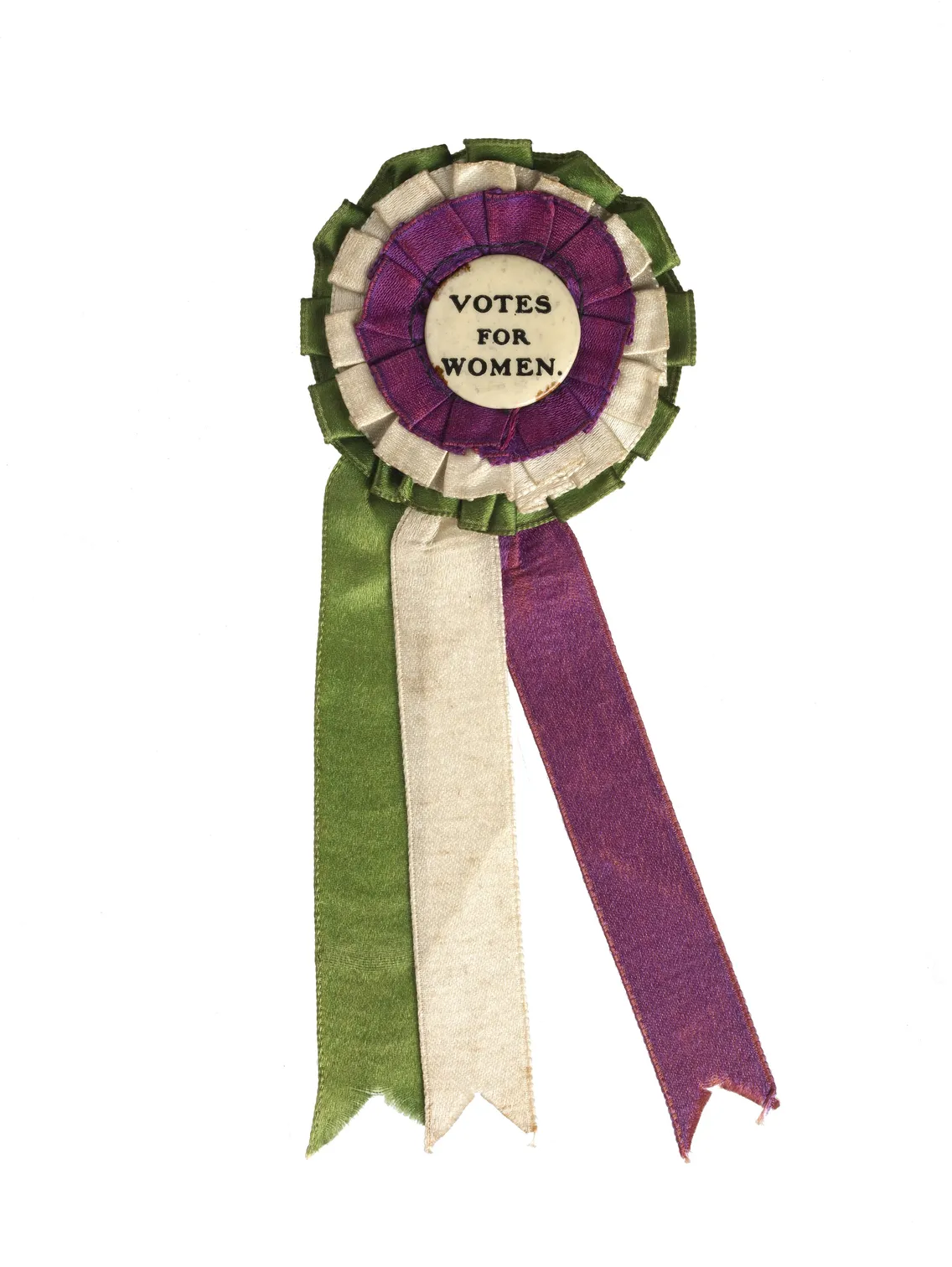 A vintage "votes for women" suffrage ribbon in green, purple, and white, featuring a rosette and two hanging ribbons.