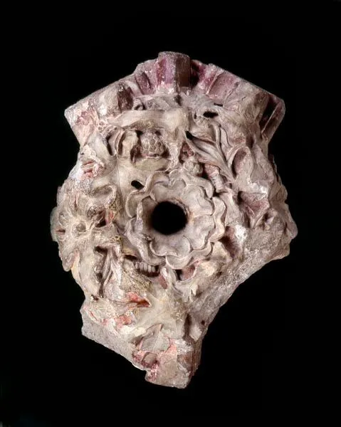Ancient carved stone capital with intricate floral designs and a central circular hole, against a black background.