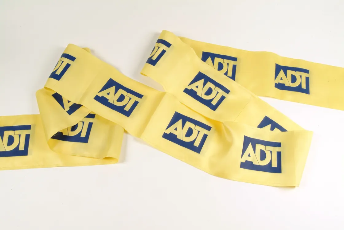 Yellow barrier tape with "adt" printed in blue, spread and overlapping on a white surface.