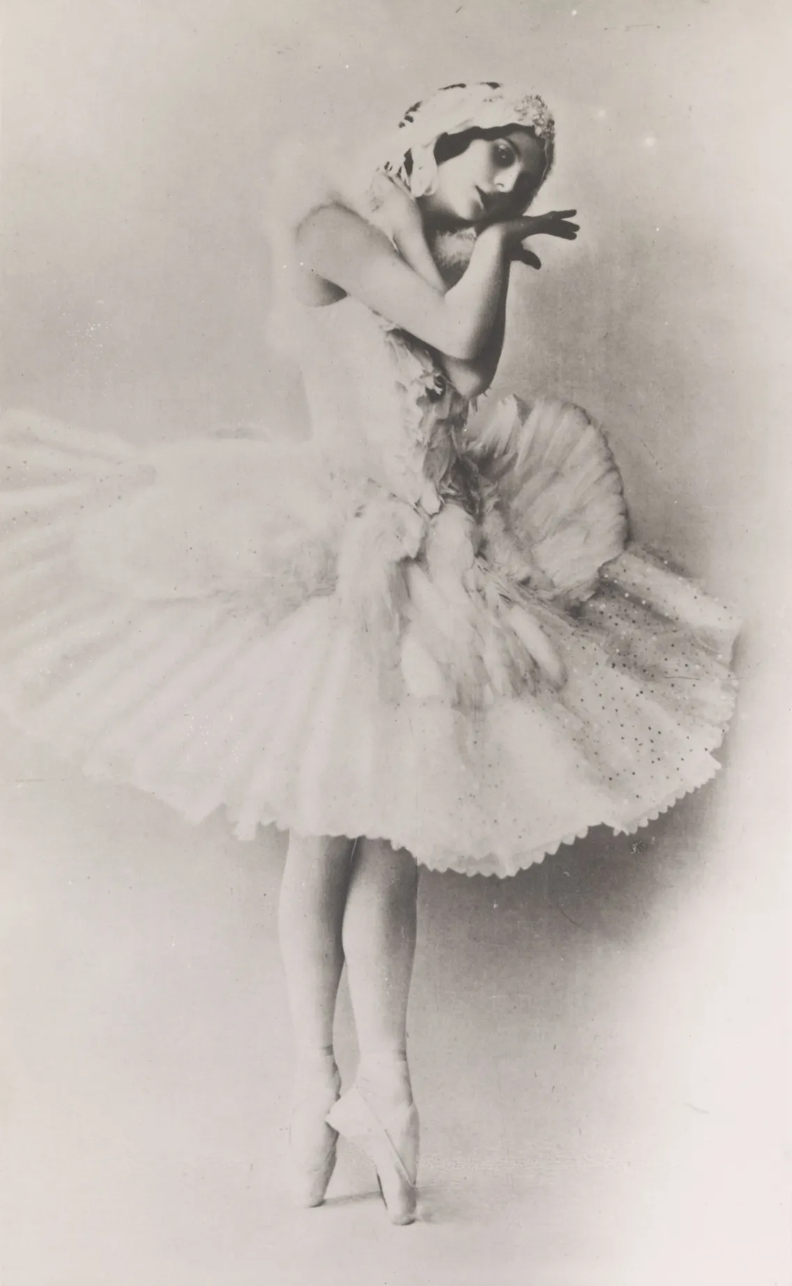 Vintage black-and-white photograph of a ballerina posing elegantly in a tutu and ballet pointe shoes, wearing a headband.