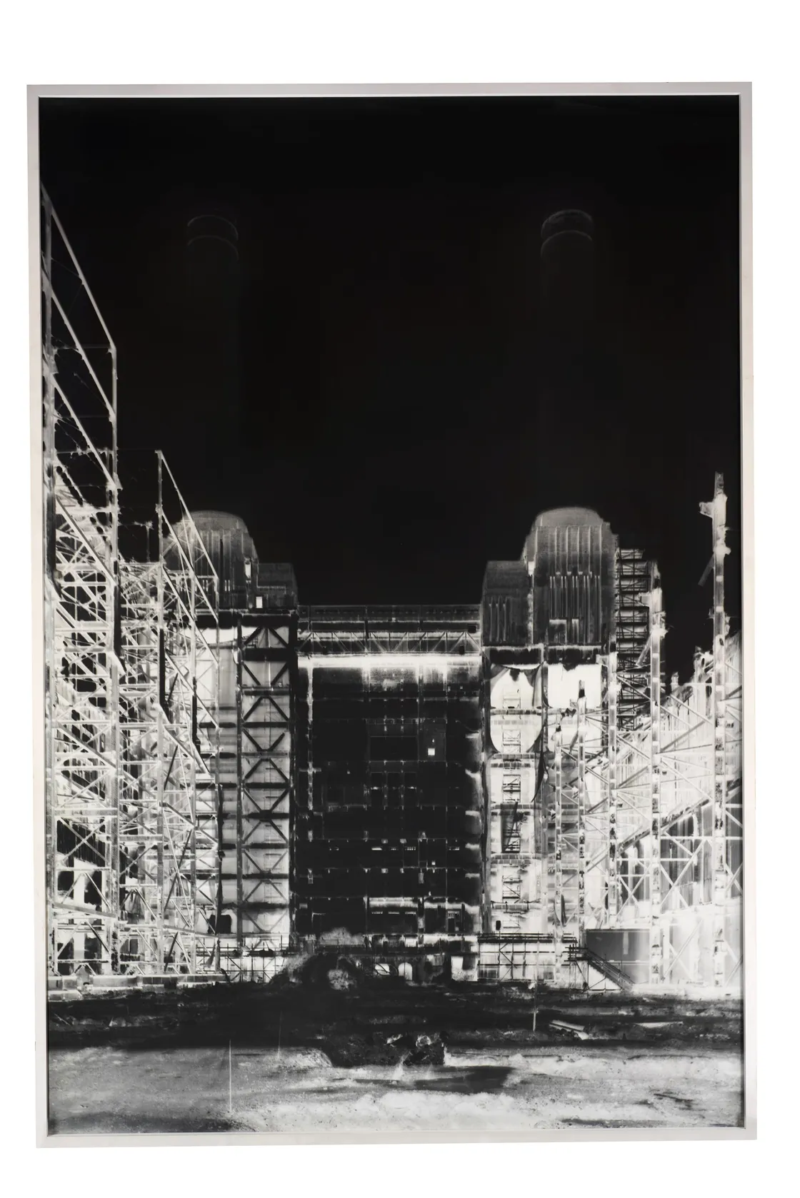 Black and white photograph of a large industrial structure at night, featuring two prominent towers and a complex network of scaffolding and supports.