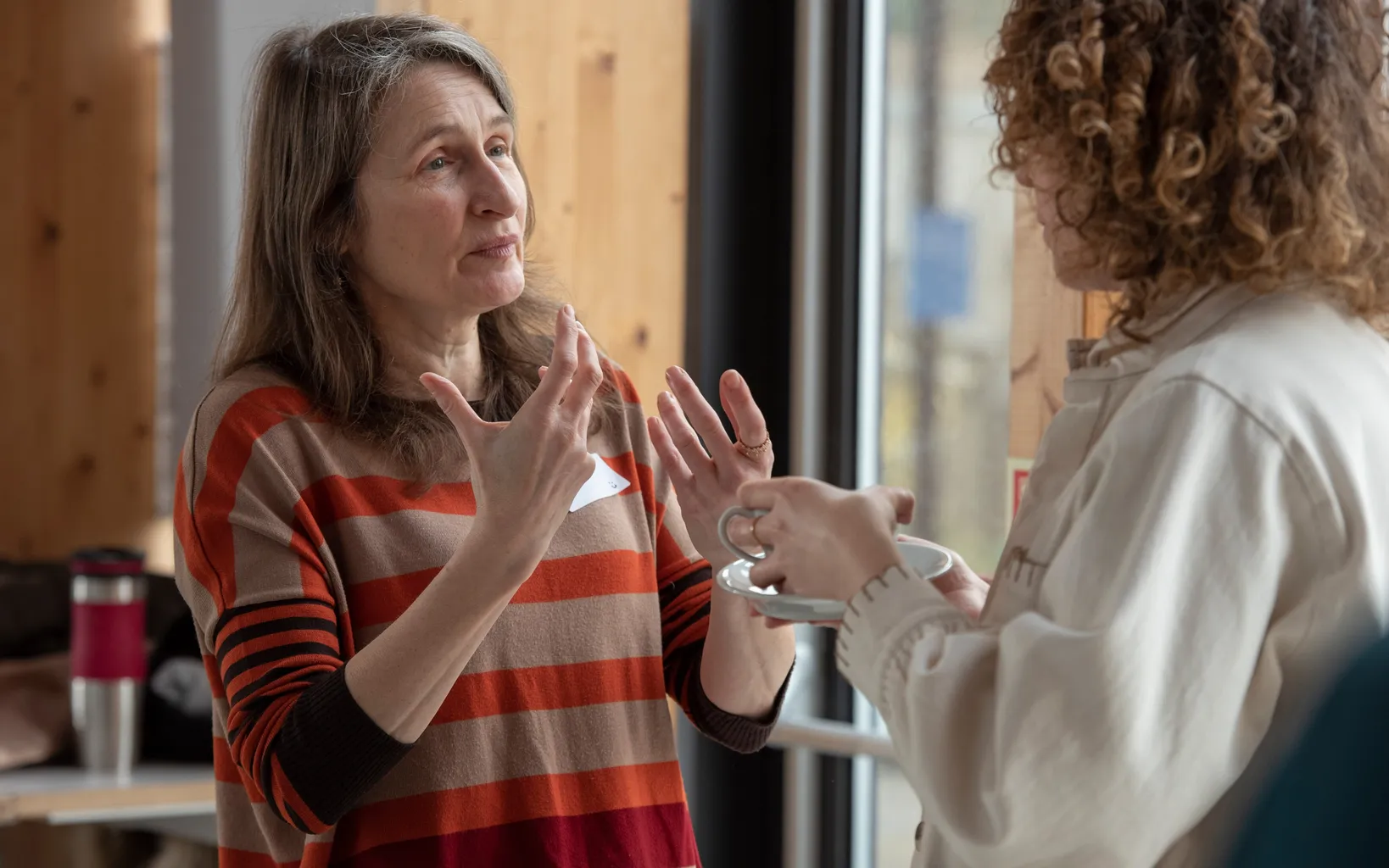 Two people engaged in a conversation, one gesturing with hands while the other holds a cup.