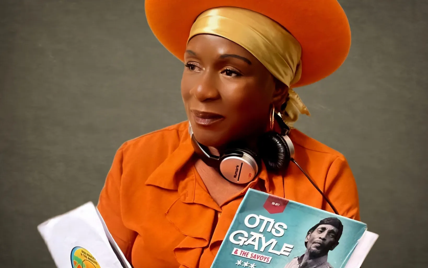 A woman in an orange outfit and hat holds vinyl records and wears headphones around her neck, embodying the signature style of Melvina Moves. A "DJ Melvina Moves" logo is in the upper left corner.