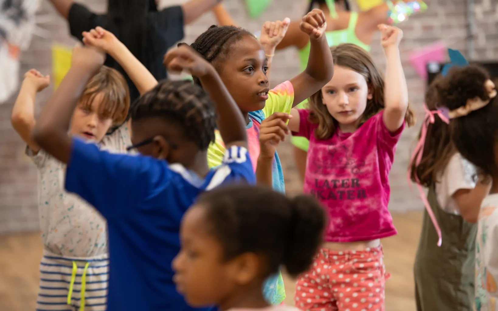 A group of children stand with arms raised, participating in a lively dance or movement activity indoors, bringing the joyful spirit of a Caribbean festival to life.