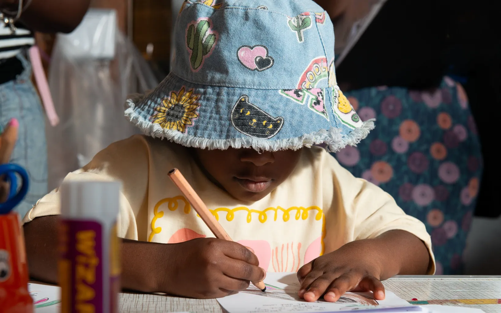 Children sitting at a table engaged in a craft activity, surrounded by art supplies.