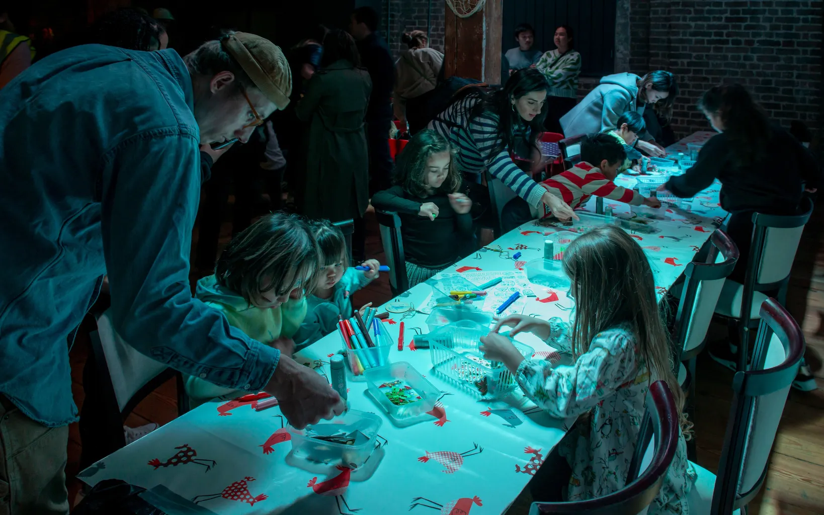 People gathered around a long table decorated with a festive tablecloth, engaging in arts and crafts activities.