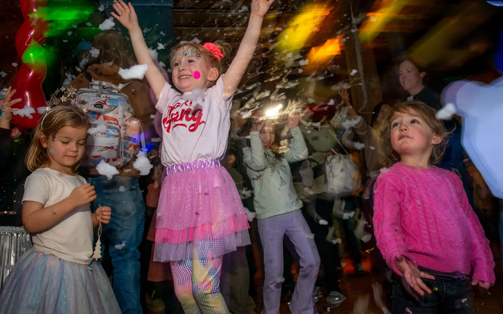 Bubbles and colourful balloons float above a crowd of families dancing within a historic warehouse.