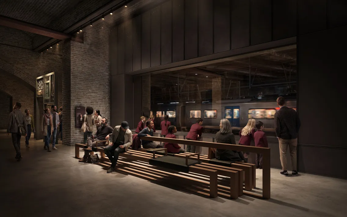 People are sitting and standing on benches in a dimly lit indoor area of the general market, looking through a large window at a moving train on the platform outside.