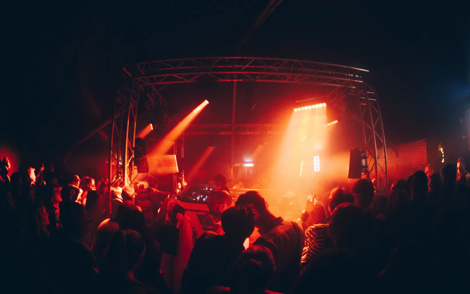 A club scene with orange and yellow lights in a dark setting and stage in the back