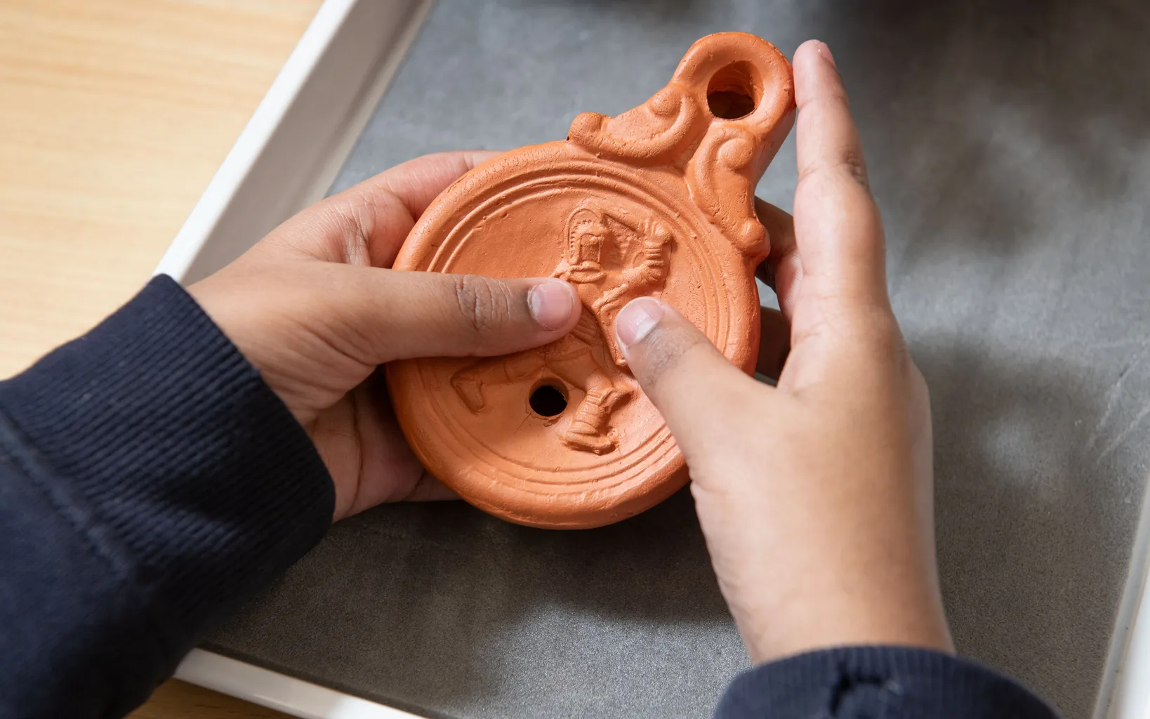 A person holds a round, terracotta oil lamp with a figure engraved on its surface.