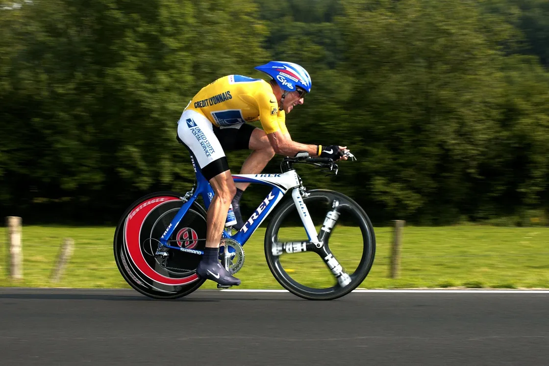 A side photograph of a man cycling and wearing cycling gear on a road, with motion blur in the scene behind him