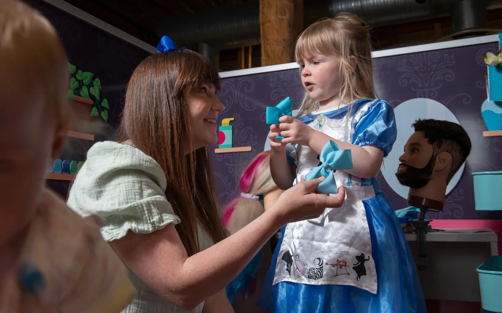 A woman is kneeling on the floor next to a small child wearing blue fancy dress.