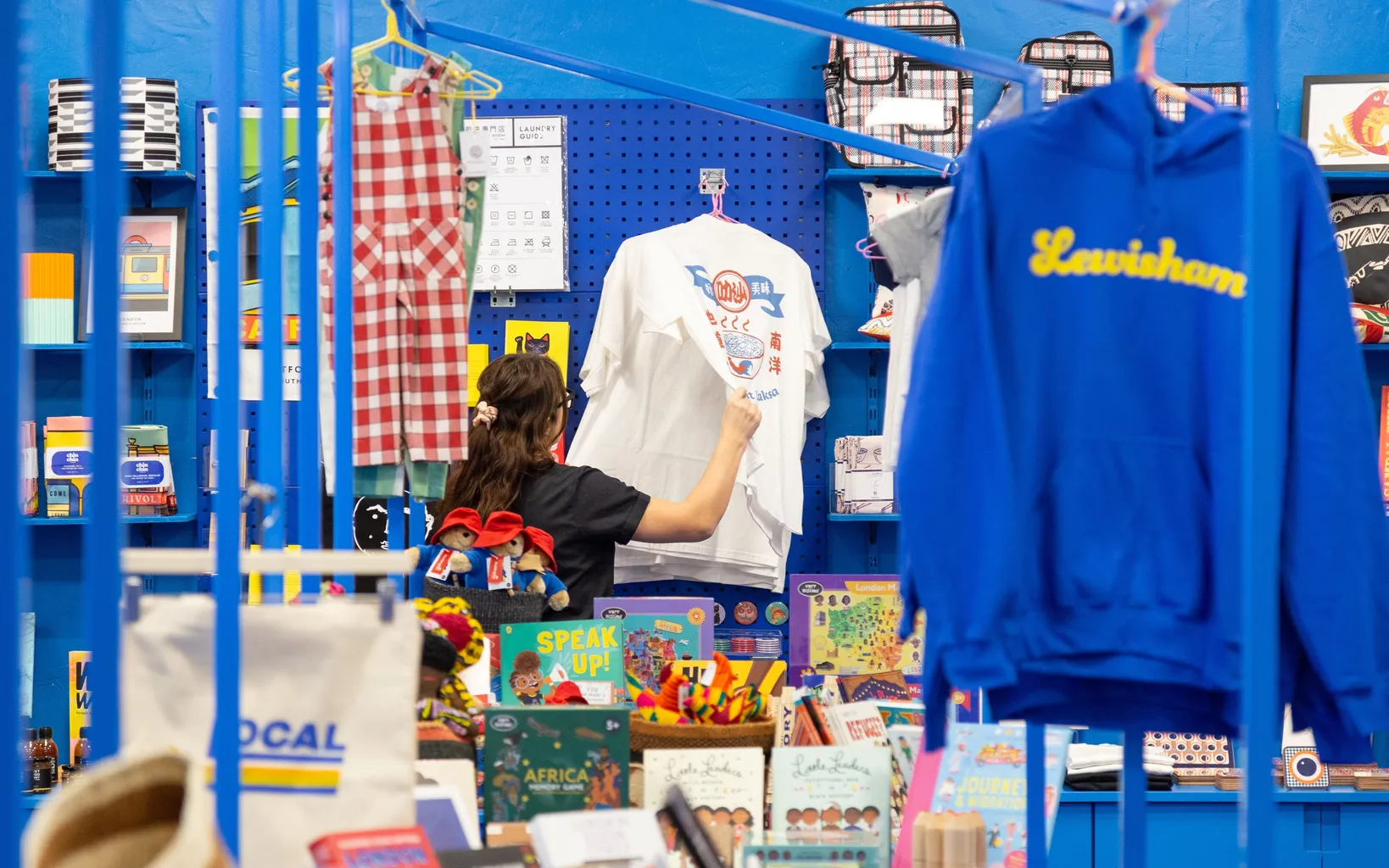 A woman browses a colourful blue market stall, where t-shirts, books and other goods are on display.