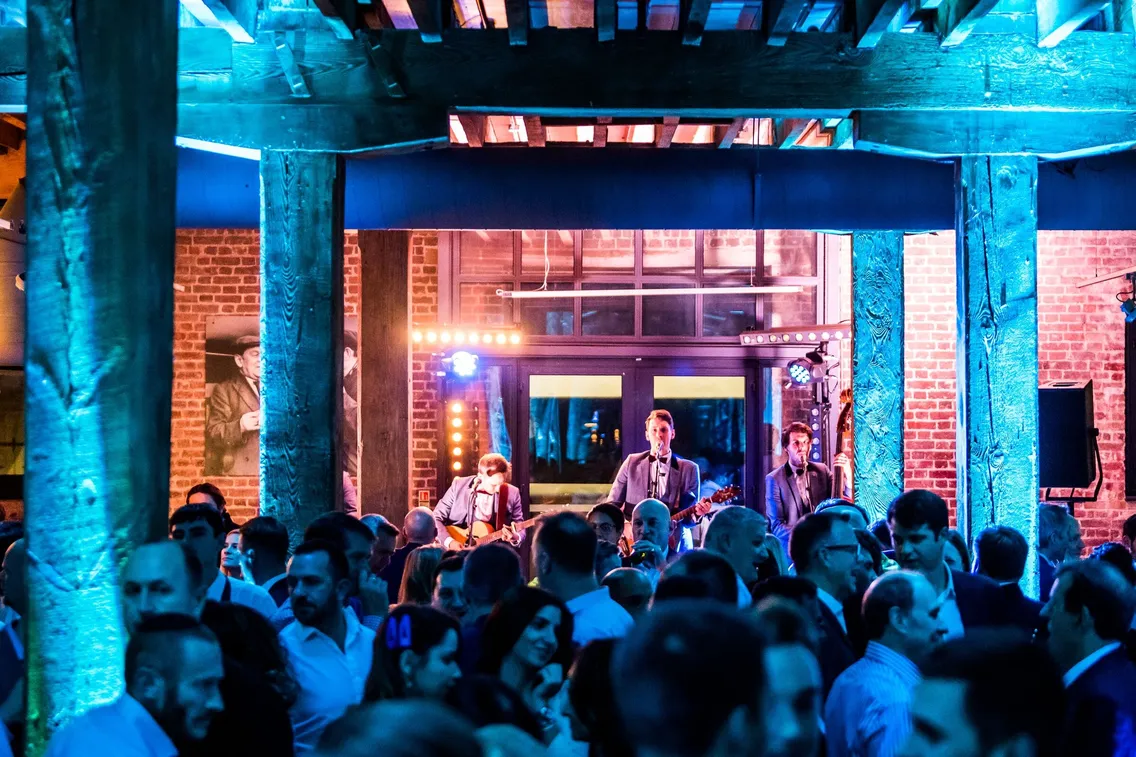 Band performing on stage in a lively venue with blue lighting, surrounded by a crowded audience.