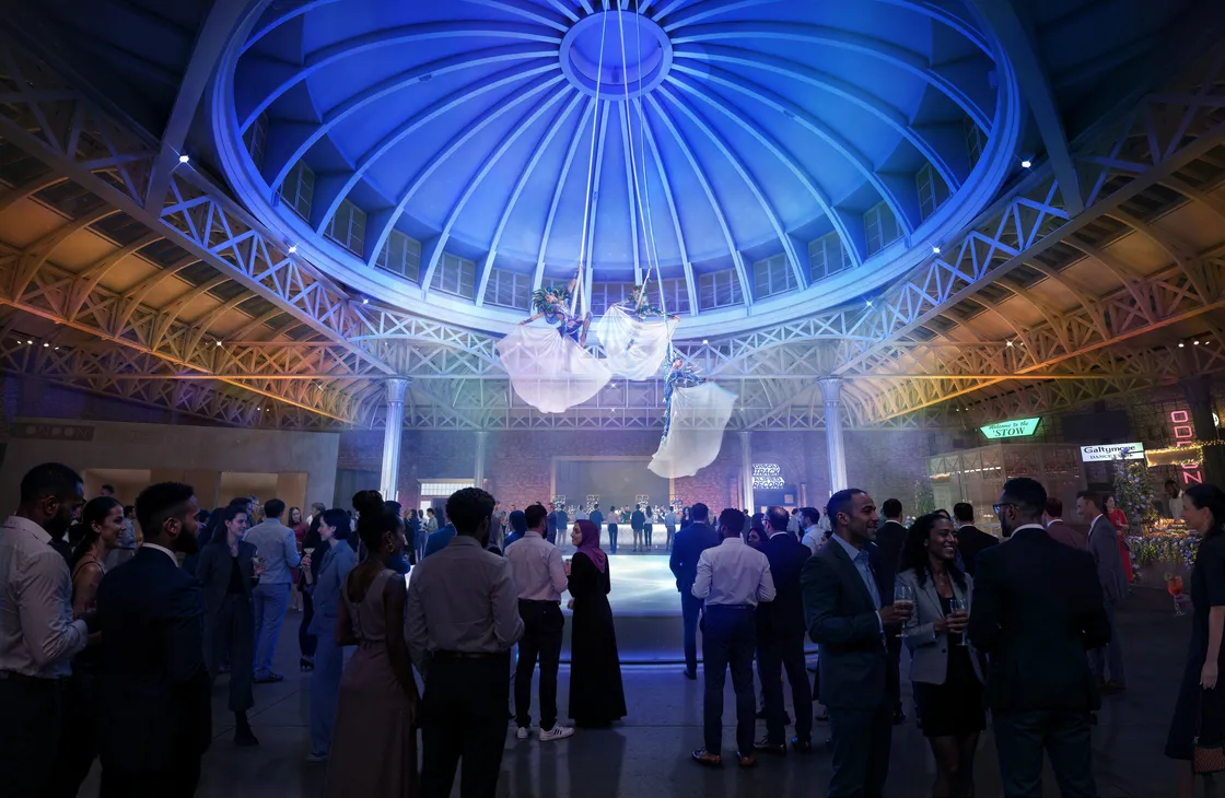 A crowd of people dressed in formal attire gathers under a large, dome-shaped, blue-lit ceiling at an indoor event venue.