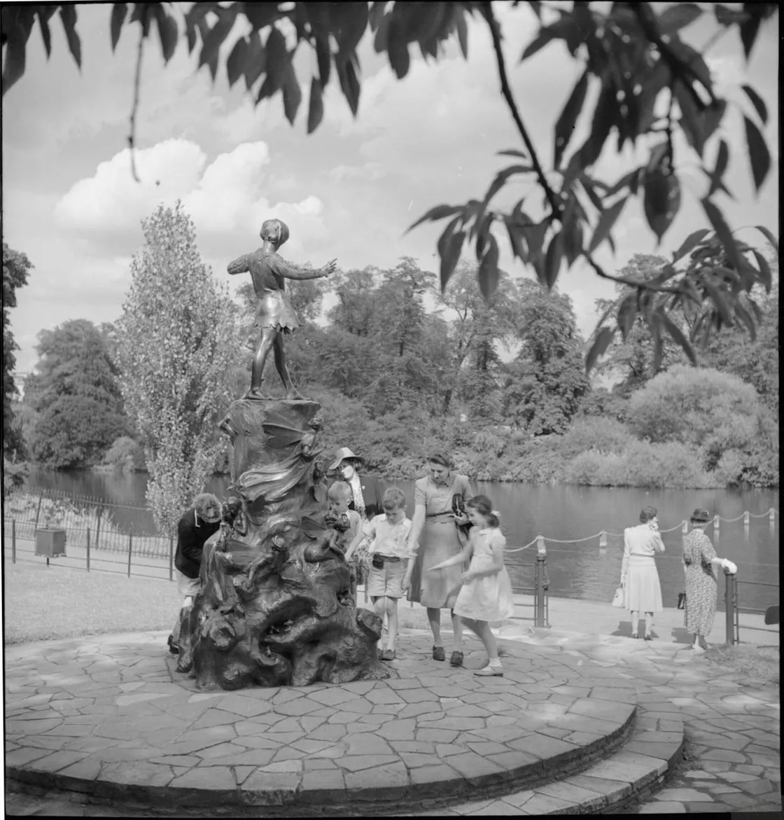 A family standing by and investigating a statue featuring a large decorative plinth with a small boy on top, and a lake in the background