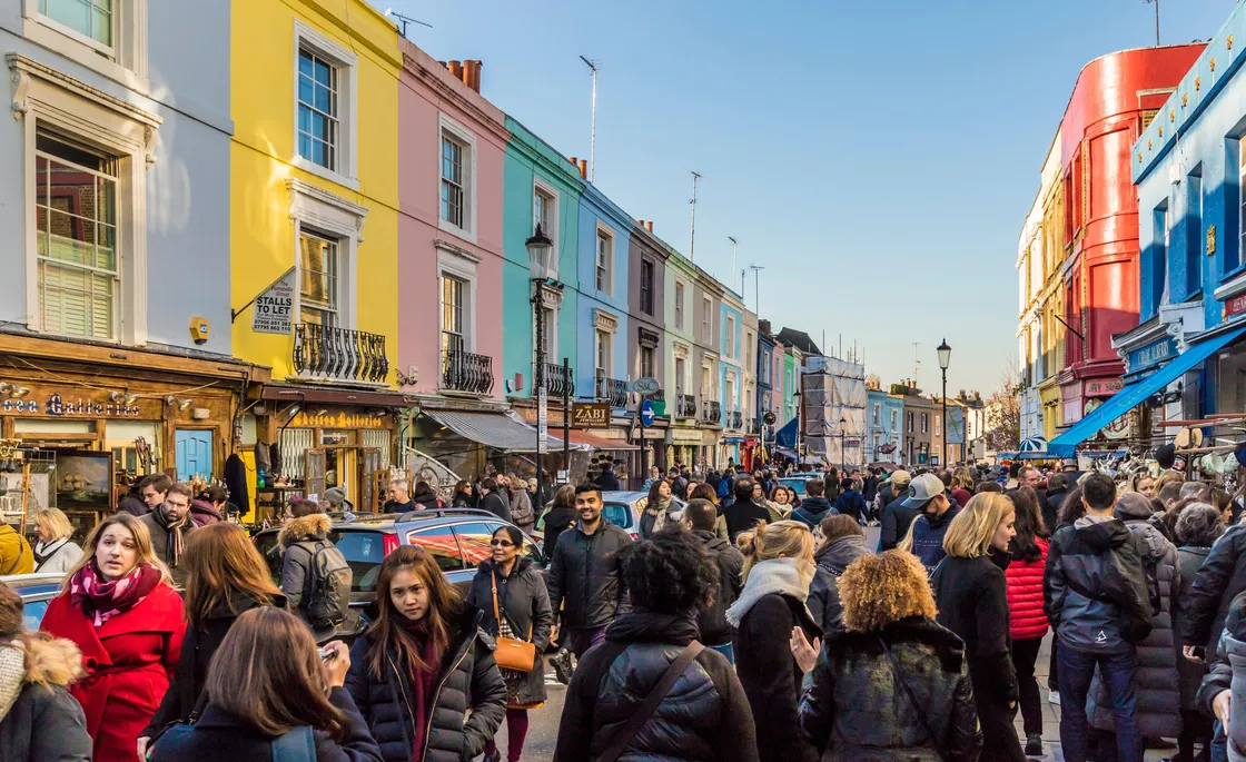 A large crowd of people in a street market lined with colourful buildings and a blue sky