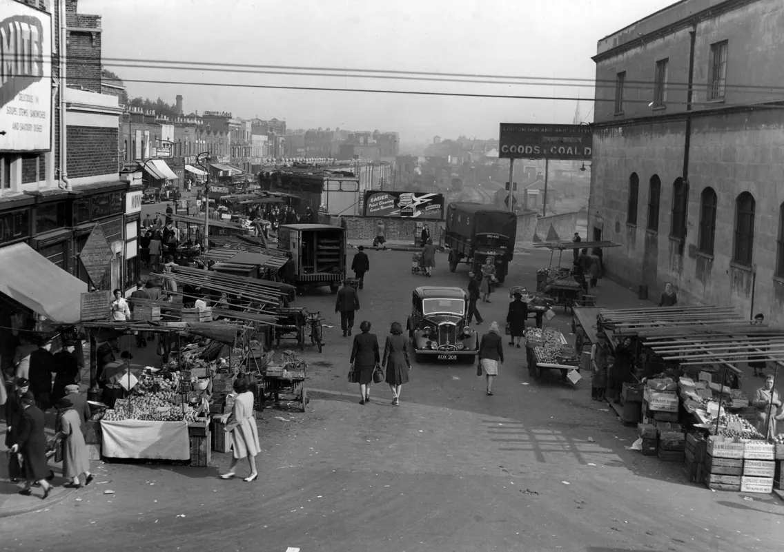 People walking away from the camera in a market setting with residential buildings seen in the background