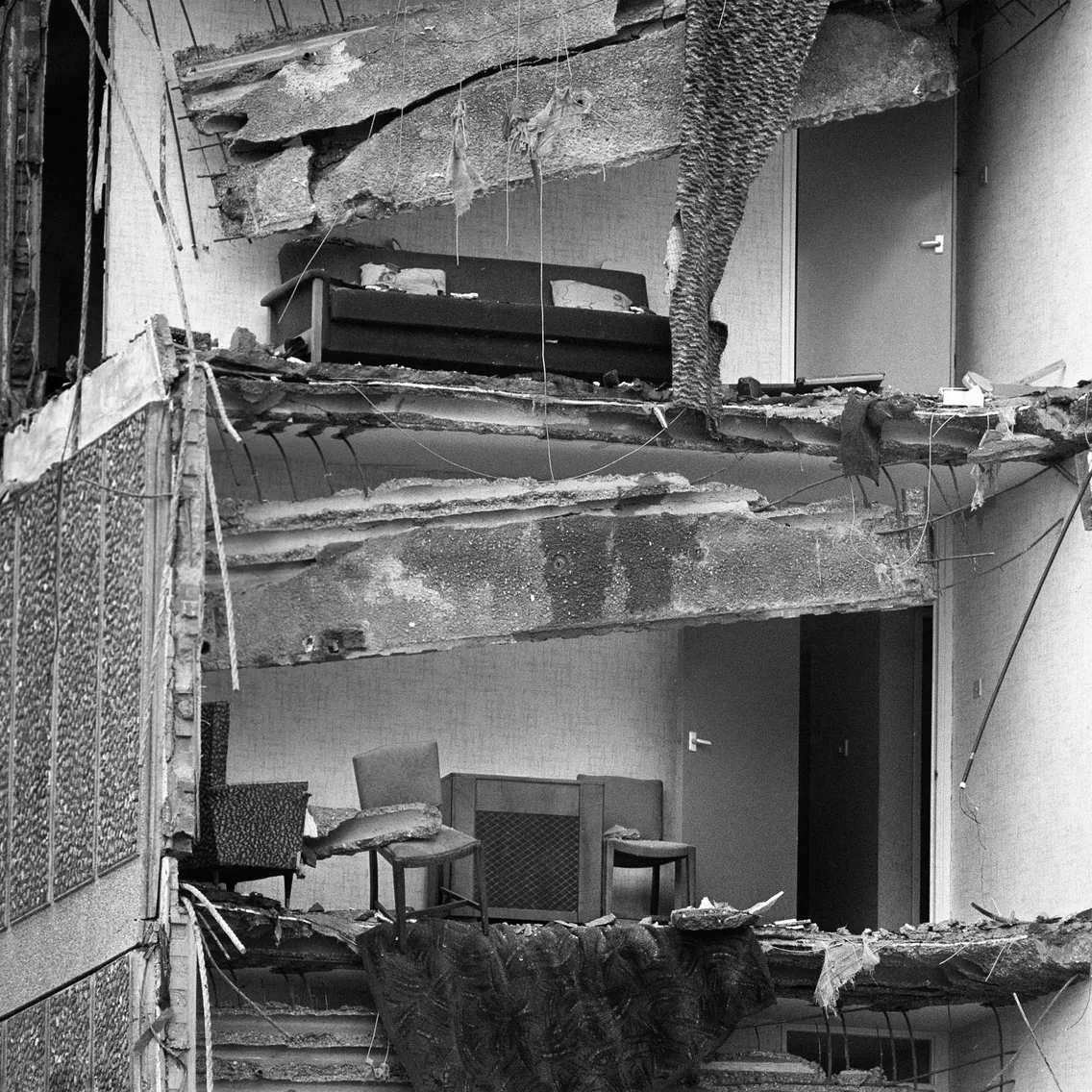 A damaged building with a wall missing showing two living rooms atop each other in a tower block