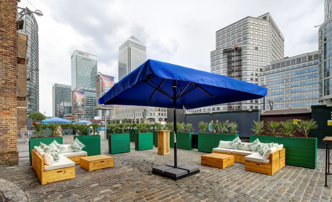 An outdoor terrace with yellow seating, a blue umbrella and city skyrises in the background