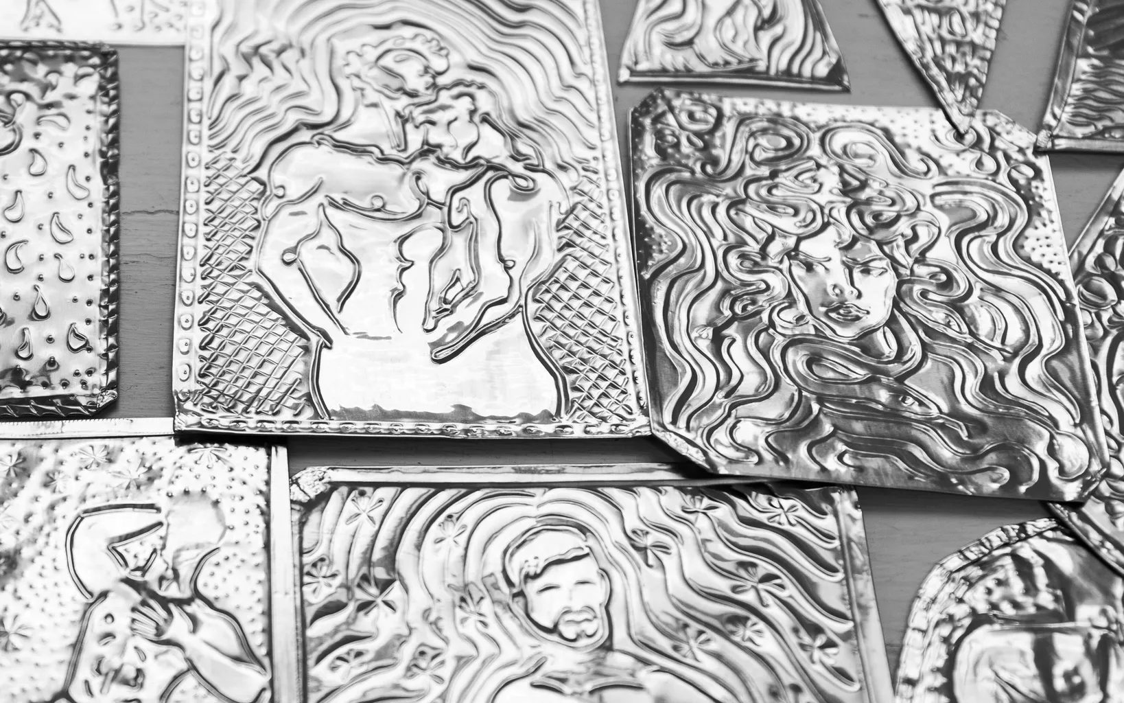 Several small sheets of metal with embossed intricate images, including of Medusa and two men in an embrace