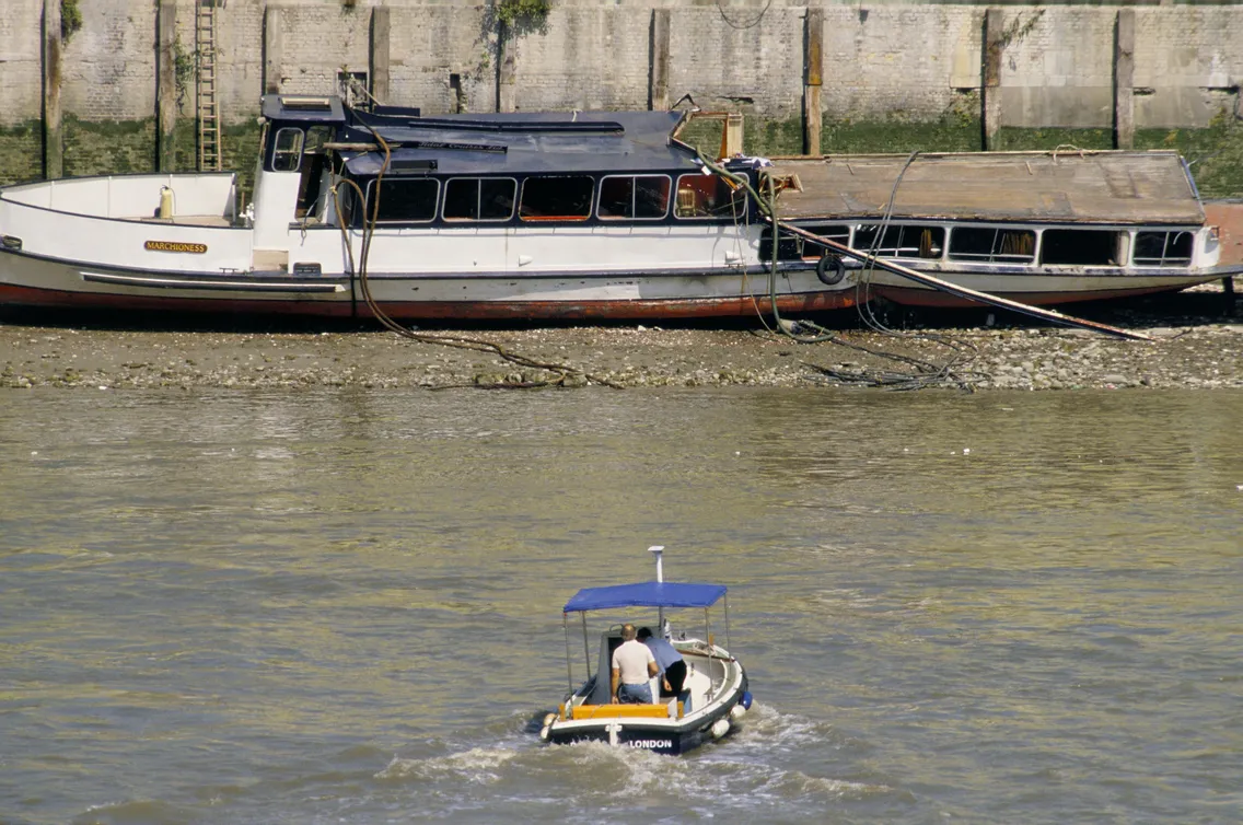 A small boat with a person in moving towards a larger boat in the background of the water