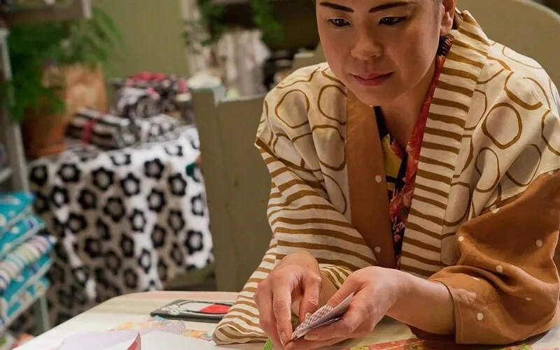 Three women in elaborate, traditional costumes and feathered hats standing outside a building, one eating and another drinking from a cup.