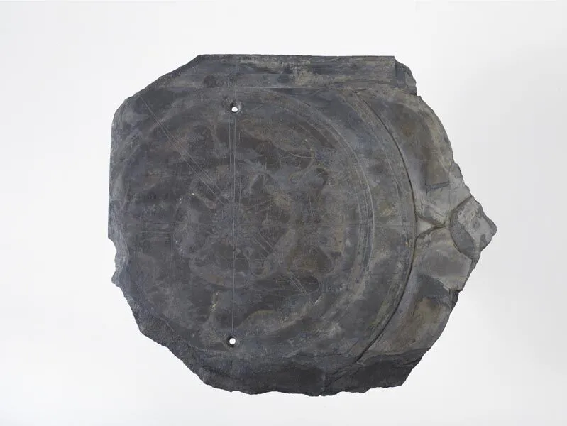 Ancient circular artifact with intricate engravings, mounted on a light grey background.