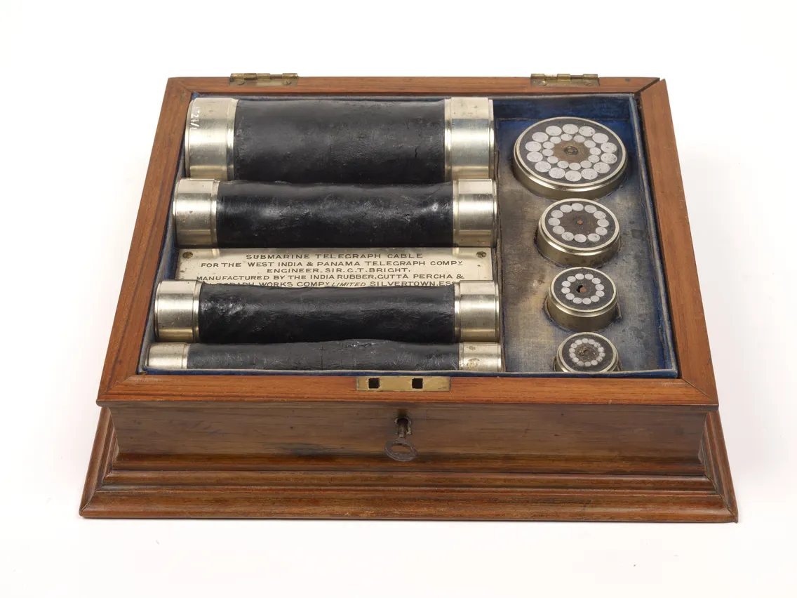 Vintage submarine telegraph cable samples displayed in a wooden box, alongside various components and intricate labels.