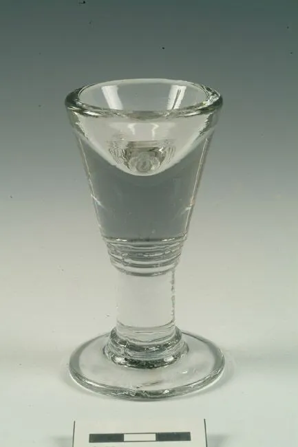 Clear glass flute with a thin stem and a wide, rounded bowl, filled with a clear liquid, displayed against a light background.
