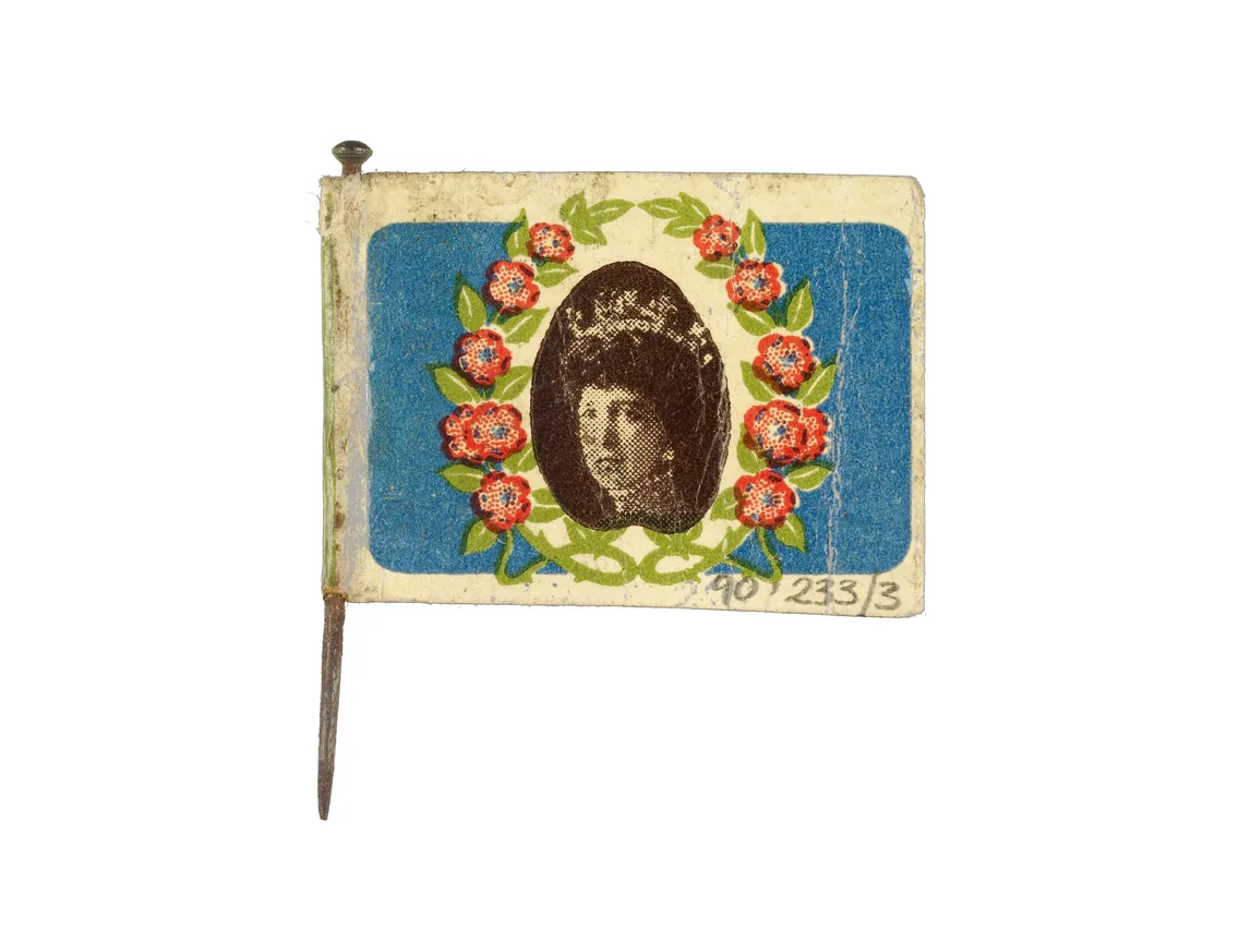 Vintage pin featuring a portrait in an oval frame surrounded by flowers, set against a blue background, mounted on a small flagpole.