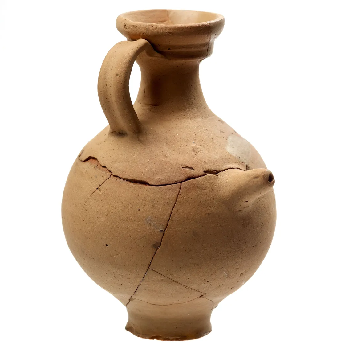 An ancient clay vessel with a handle and a spout, showing visible cracks and missing pieces, stands against a white background.