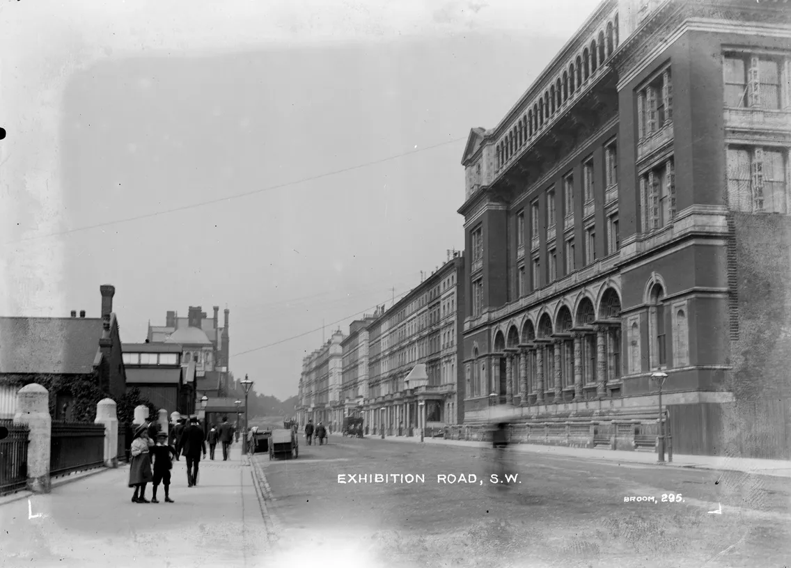 Historical black and white photo of exhibition road, s.w., showing the facade of a stately building with pedestrians walking along the sidewalk.