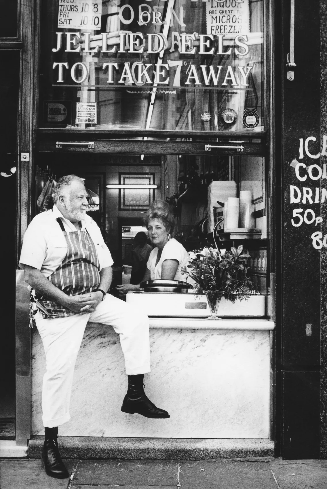A man sat on the outside of a window ledge with 'Jellied eels to take away' on the window