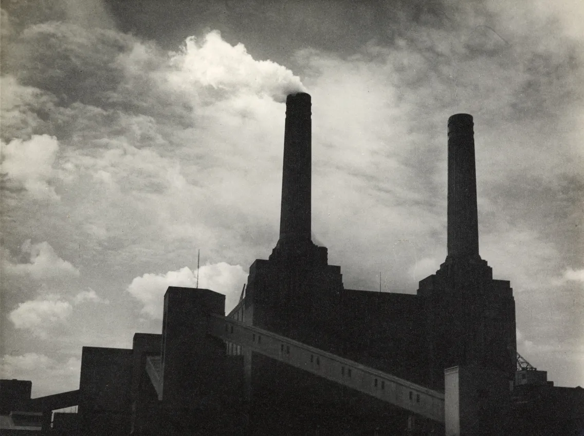 Black-and-white image of an industrial building with two large chimneys against a cloudy sky.