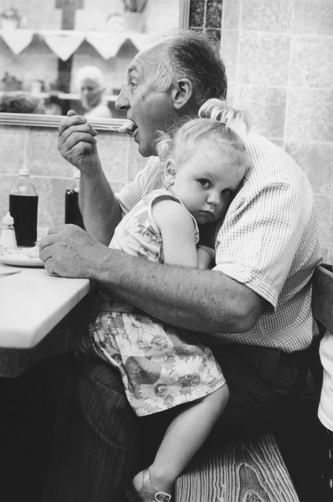 A man eating food while a little girl sits in his lap and looks towards the camera