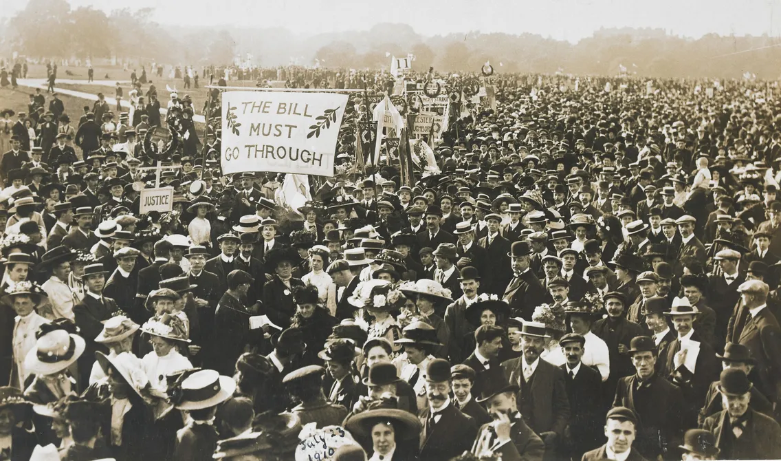 Historical black and white photo of a large crowd at a political rally, with people holding signs including one that reads "the bill must go through.