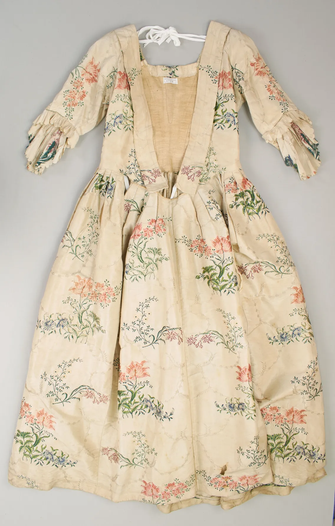A cream silk dress with a floral pattern on a grey background