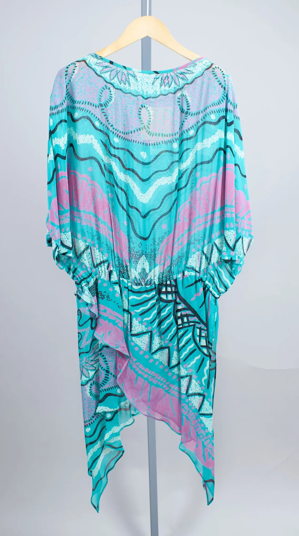 A long, sheer, turquoise and pink printed kaftan with loose sleeves and an abstract asymmetrical hem, displayed on a hanger against a plain background.