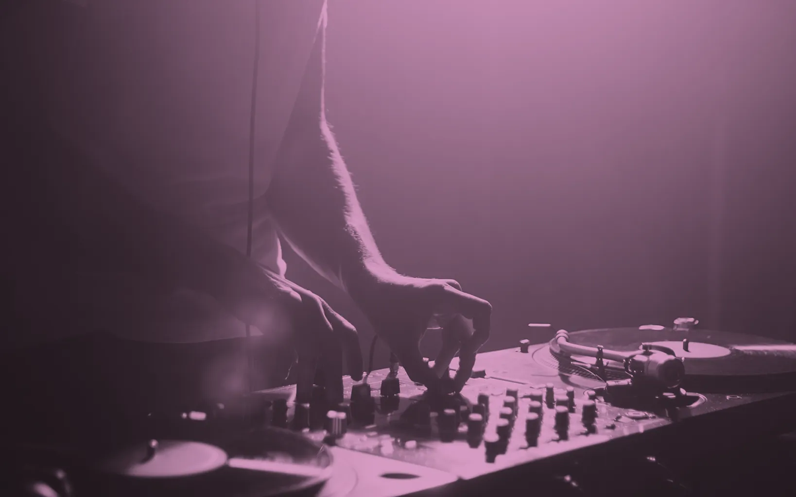 A person adjusts controls on a DJ mixer and turntables in a dimly lit setting, with strong contrast between light and shadow, creating the perfect atmosphere for a striking photo with a purple tint