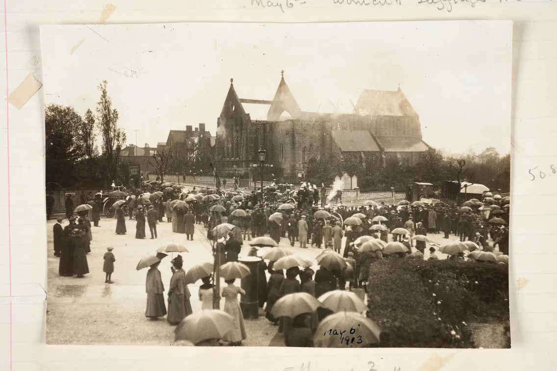 Historic photo of a crowd with umbrellas gathered in front of a grand castle-like building, possibly from the early 20th century.