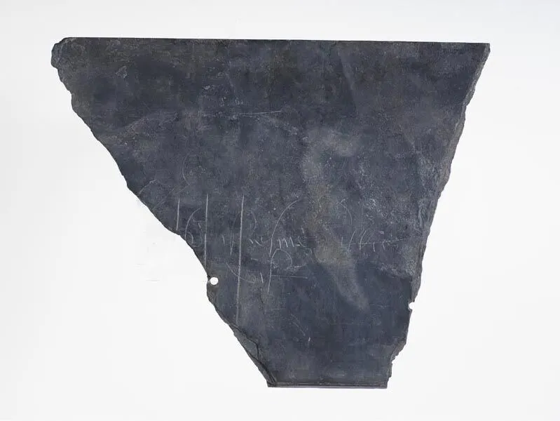 A fragment of a dark slate with faint, illegible white inscriptions, displayed against a white background.