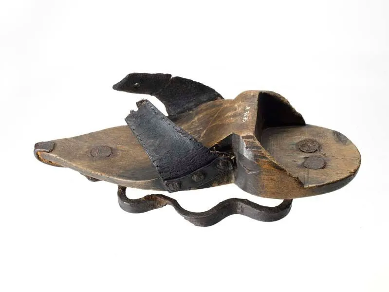 A wooden shoe with leather straps and attached metal components, showing signs of wear and age.