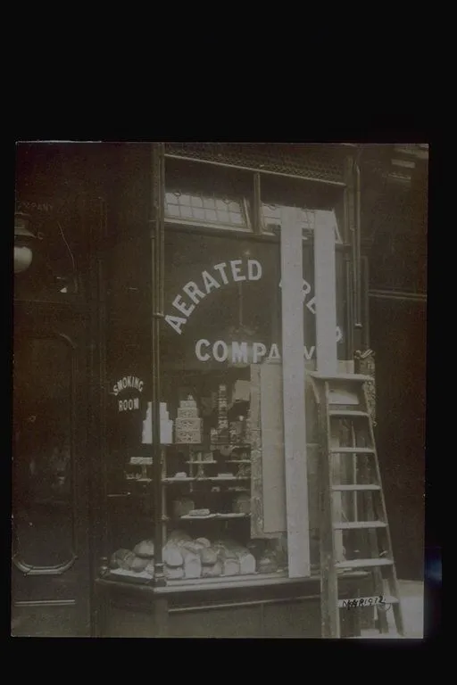 Black and white photo of a bakery storefront labeled "Aerated Bread Company," with bread displayed in the window and a wooden ladder leaning against the glass.