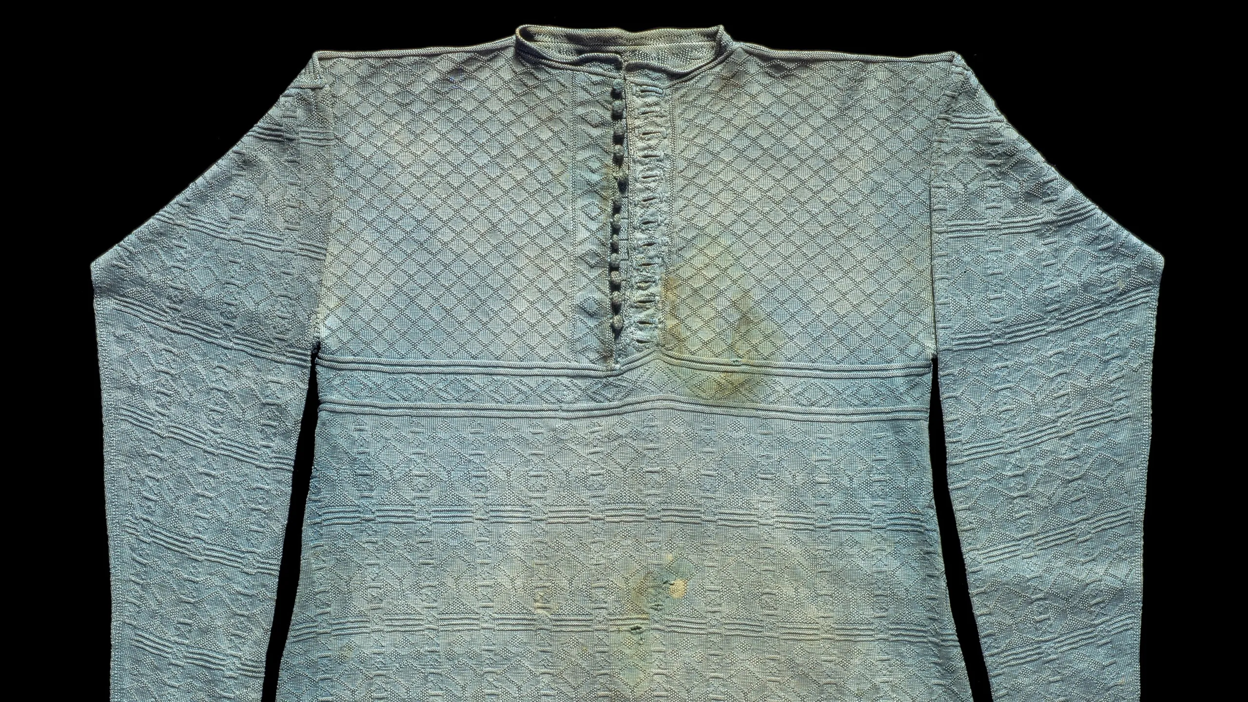 Knitted pale green (watchet?) silk vest or waistcoat said to have been worn by Charles I at his execution. Repeating geometric pattern, long sleeves, trapezoid shape to the body. Central front opening with buttons, bottom row and buttonholes faced with self-coloured tabby silk. Probably produced in England, possibly in or around London, of Italian silk.